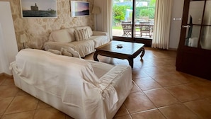 A living room with a stone wall, a sofa, a coffee table, and a view of the outdoors through a glass door. - Villa Noray Cala Morell (Cala Morell)