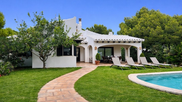 A white house with a patio, a swimming pool, and a garden. - Villa Noray Cala Morell (Cala Morell)