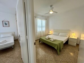 Une chambre d’hôtel avec un lit, une table de chevet, un ventilateur de plafond, une fenêtre avec des rideaux et un tableau encadré au mur.