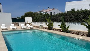 A rectangular swimming pool with clear blue water, surrounded by white walls and a hedge.