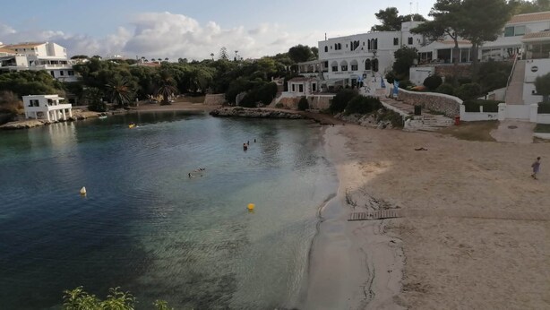 Une zone côtière dotée d’une plage de sable, d’une eau cristalline et de bâtiments blancs ornés de balcons.
