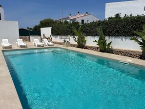 Una piscina rettangolare con acqua cristallina e azzurra, circondata da muri bianchi e un siepe.