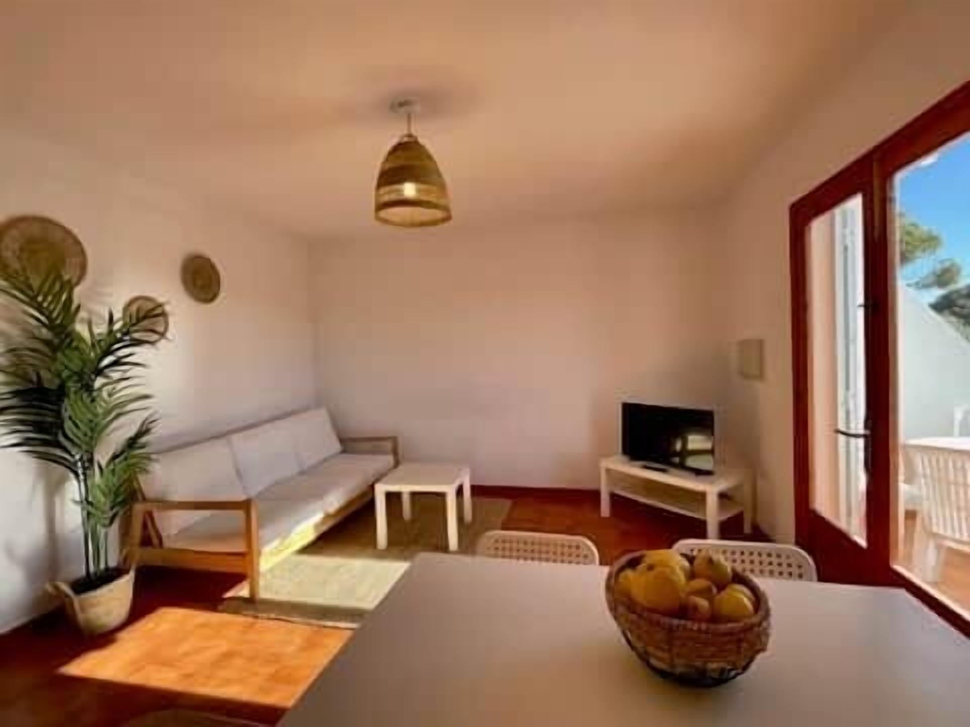 Un espacio habitable compacto con sofá, una mesa pequeña, un televisor y una mesa de comedor con una cesta de fruta.
