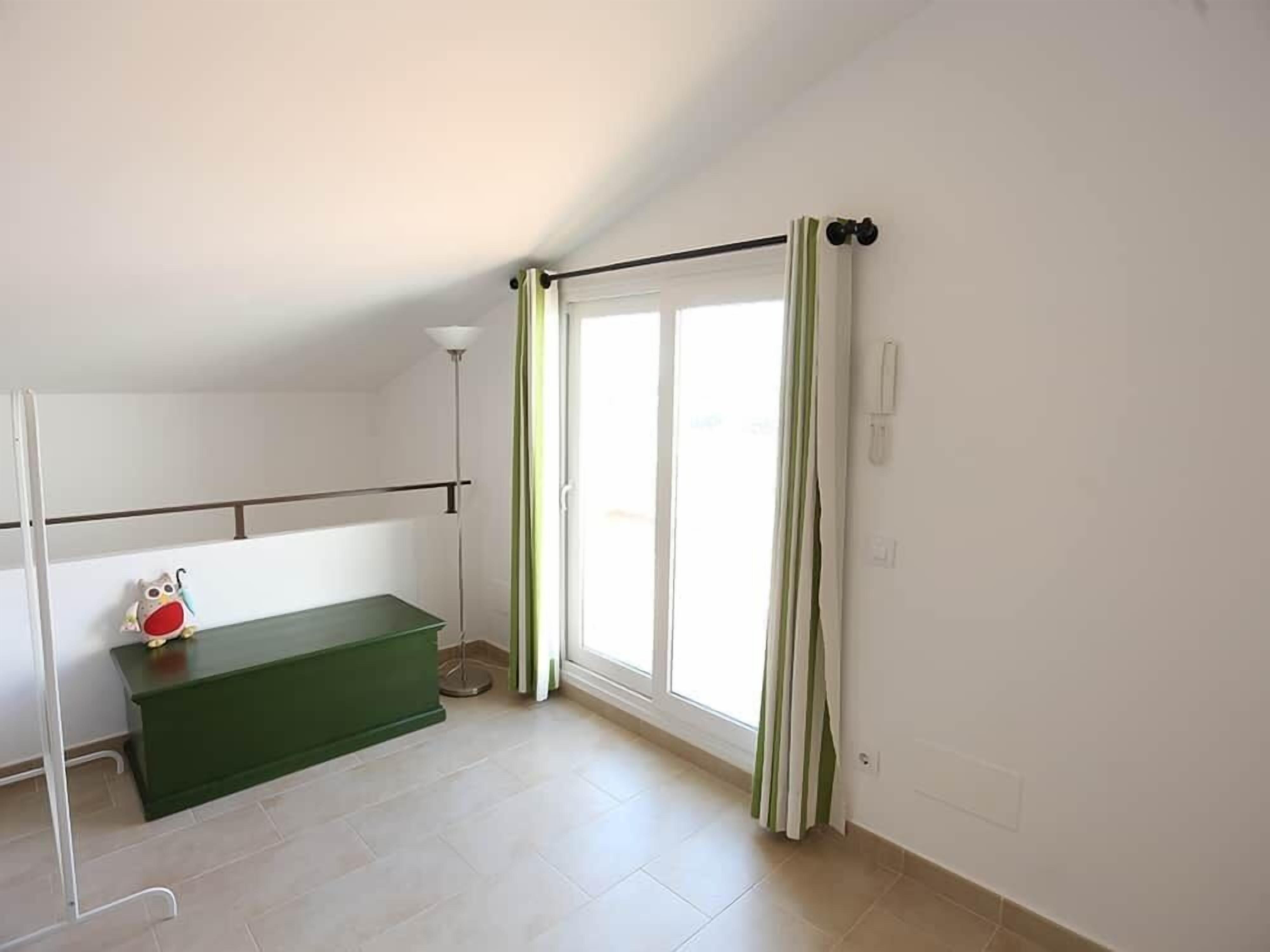 A room with a green bench, a white radiator, a floor lamp, and a sliding glass door with curtains.
