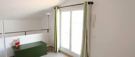 A room with a green bench, a white radiator, a floor lamp, and a sliding glass door with curtains.
