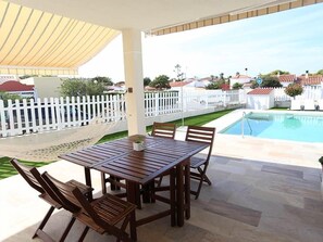 A covered outdoor patio with a pool, white picket fence, and a view of the neighborhood.