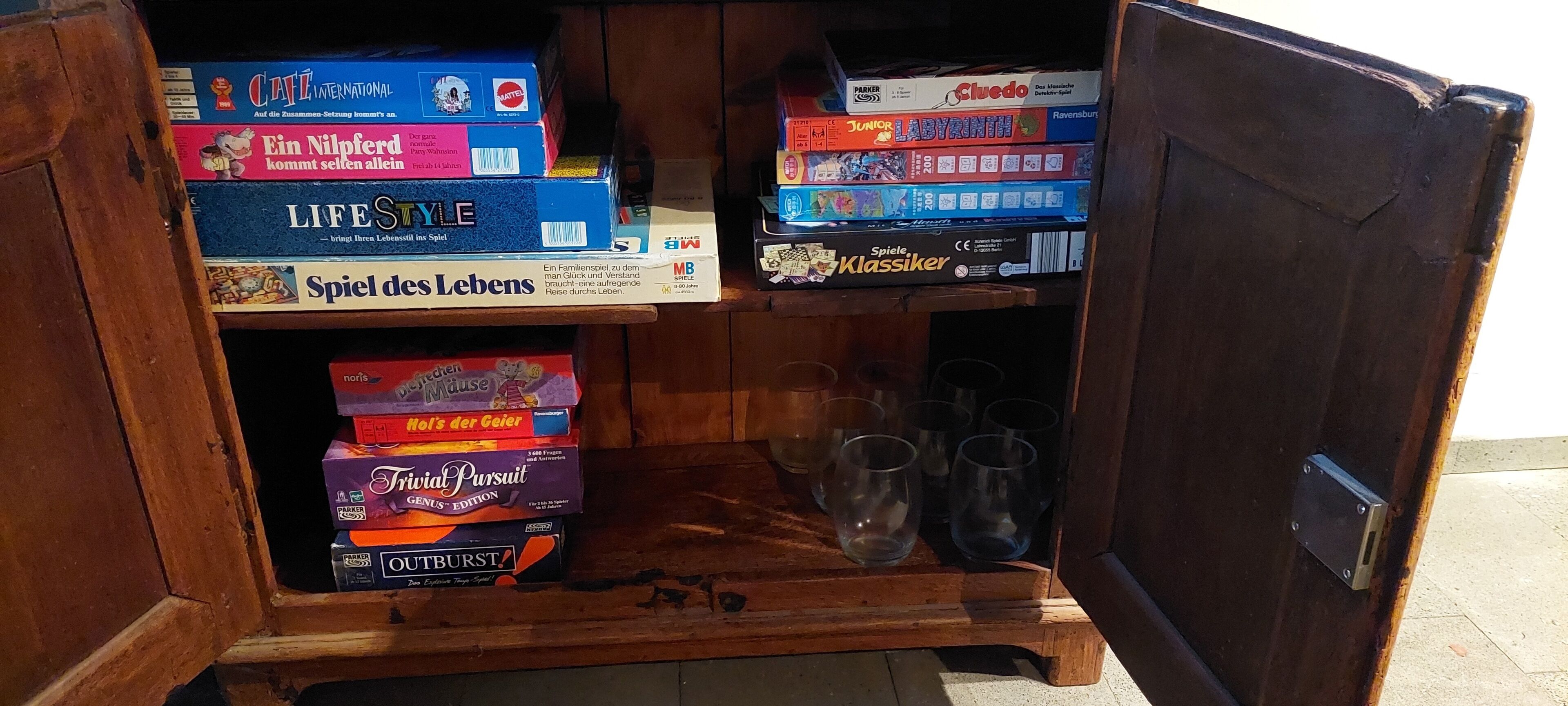 A wooden cabinet with board games and glasses.