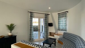 Un salon moderne avec un canapé, une table basse et un téléviseur fixé au mur. Une porte-fenêtre coulissante donne accès à un espace extérieur.