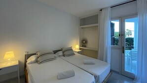 Une chambre d’hôtel avec deux lits, une petite table avec une lampe, un ventilateur et une vue sur le balcon extérieur.
