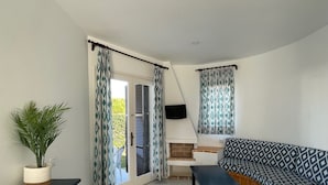 Une pièce avec un canapé, un téléviseur fixé au mur, une plante en pot et une fenêtre ornée de rideaux à motifs.