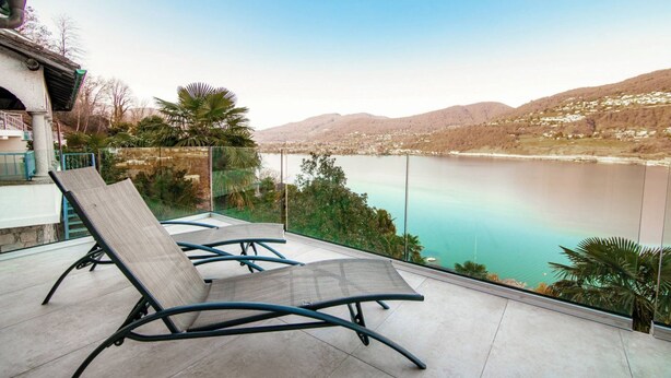 A balcony with two lounge chairs overlooking a lake and mountains.