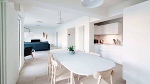 A modern kitchen with white cabinets, a dining table with chairs, and pendant lighting.