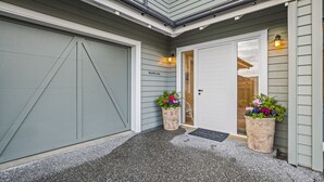 Une maison avec une porte de garage grise, une porte d’entrée blanche et deux pots de fleurs sur le porche.