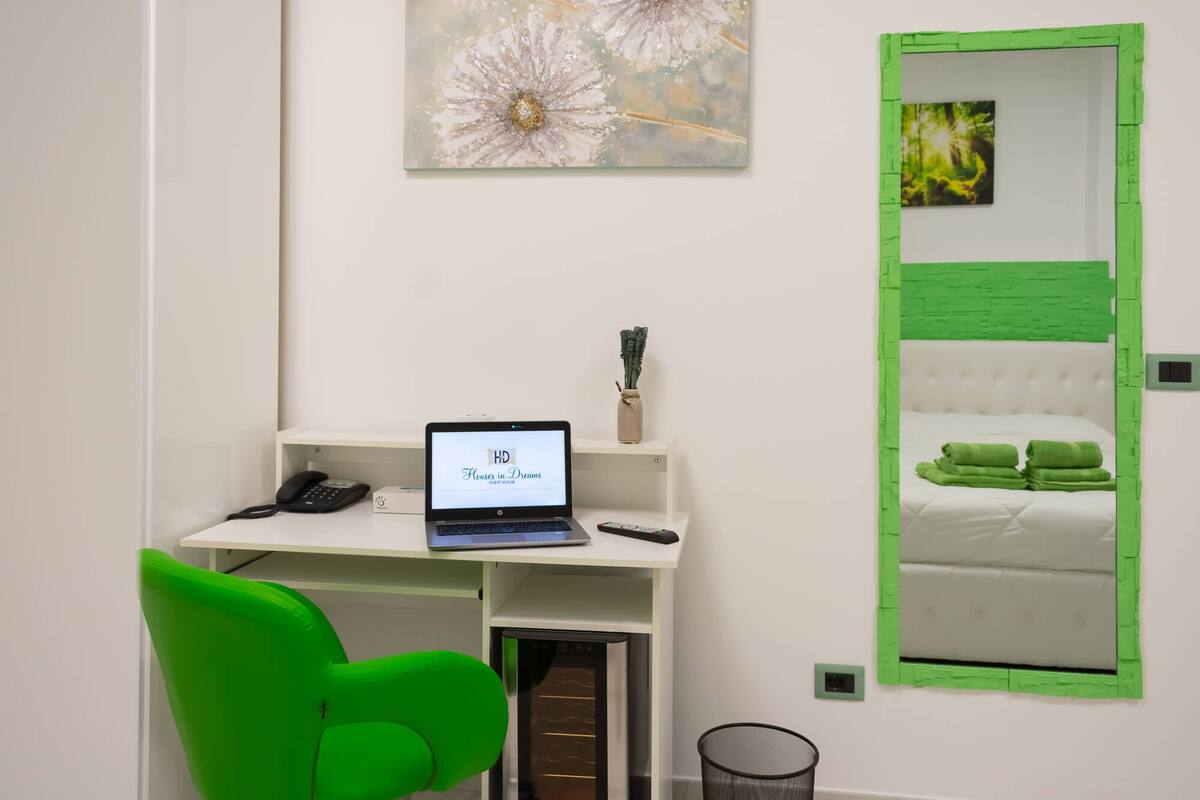 A hotel room with a desk, laptop, green chair, and a bed with green towels.