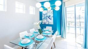 Comedor con una mesa de vidrio, sillas blancas y una pared azul de acento.