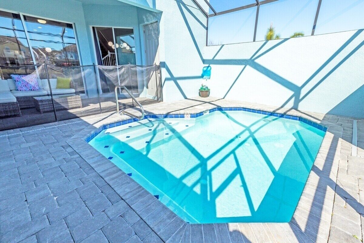 Una piscina con cerramiento de vidrio, un área de descanso con sofá y sillones, y vista a un edificio con grandes ventanales.