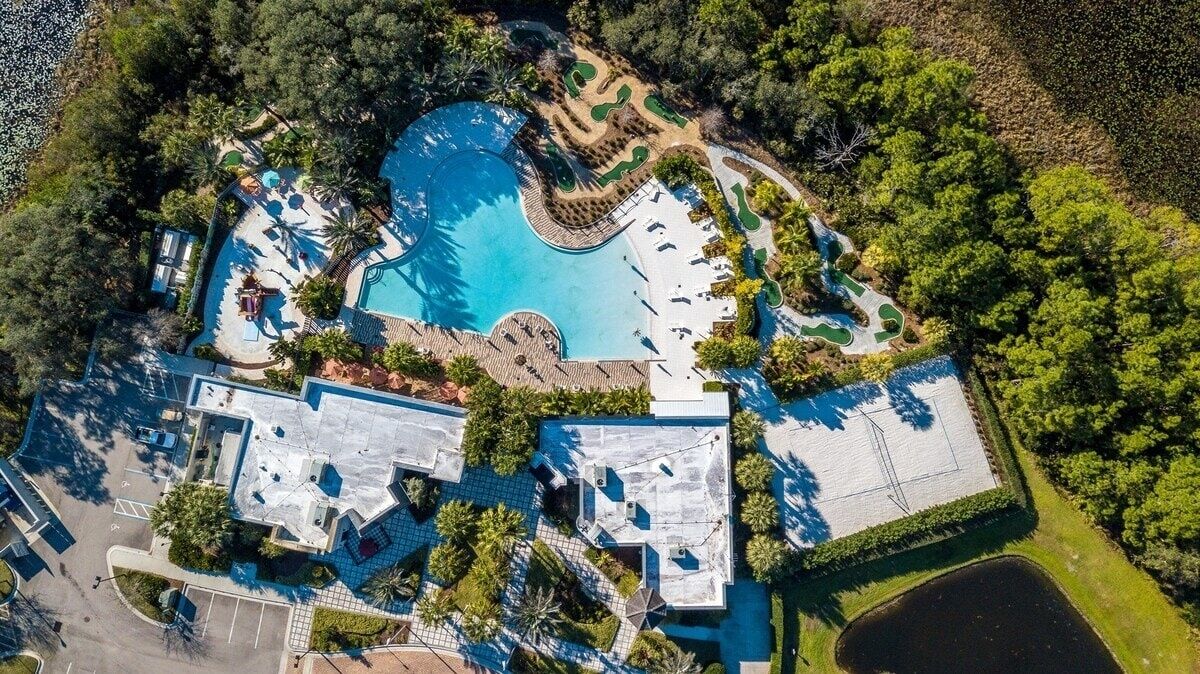 An aerial view of a resort with a large central pool, multiple guest areas, and lush greenery.