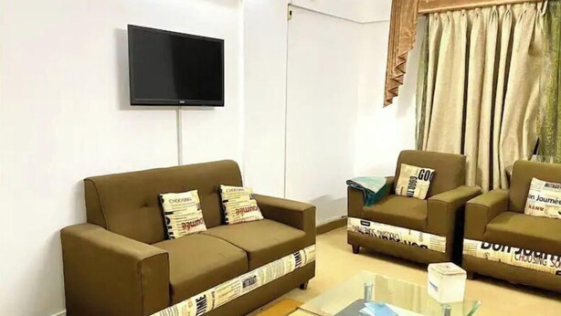 A living room with a brown sofa, two armchairs, a glass coffee table, and a flat-screen TV mounted on the wall.