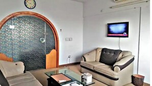 A living room with a sofa, a glass coffee table, a television mounted on the wall, and a door with a decorative glass panel.