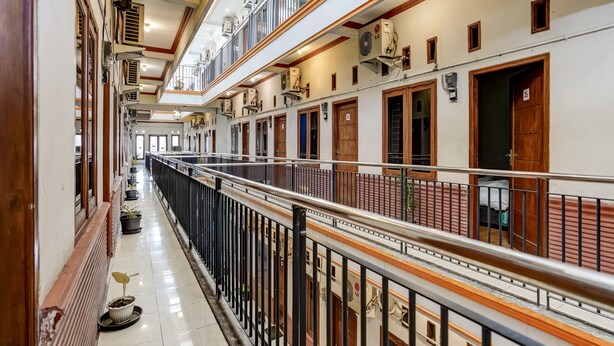 A corridor with multiple doors, a balcony with a metal railing, and air conditioning units on the walls. - Hotel O Pondok Inap Shofwa 1 (Sidoarjo)