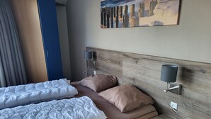 Una cama bien hecha con ropa de cama blanca y marrón, un cabecero de madera, dos lámparas fijadas a la pared y una mesita de noche de madera.