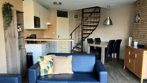 Un espacio habitable compacto con sofá, mesa de comedor, cocina y escalera.