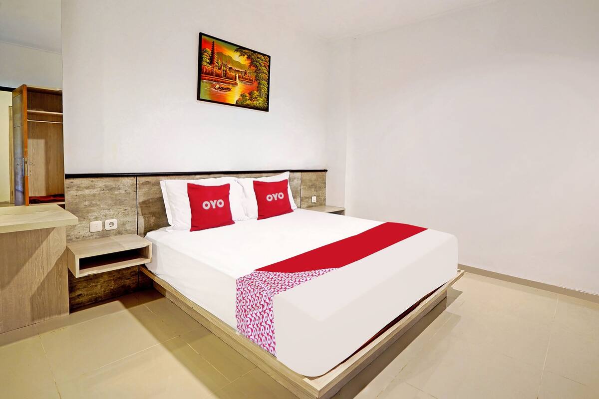 A hotel room with a bed, a nightstand, a wooden wardrobe, and a wall-mounted painting.