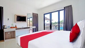 A hotel room with a large bed, a TV mounted on the wall, a desk with a chair, and a window with curtains. - Collection O 90876 Pecatu Residences (Pecatu)