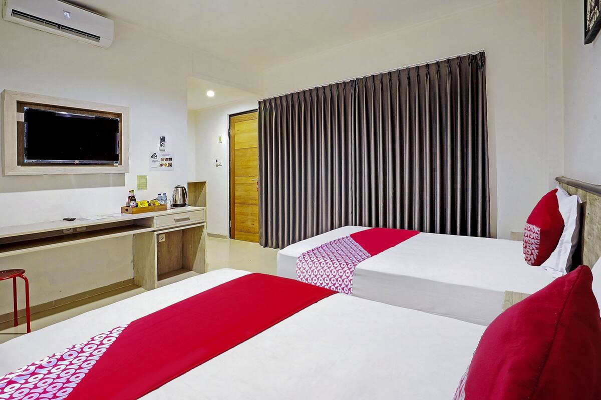 A hotel room with two beds, a desk, a television, and a window.