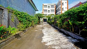 A narrow alleyway flanked by lush greenery and buildings. - Collection O 90876 Pecatu Residences (Pecatu)