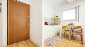 Et værelse med dør i træ, hvide skabe, et tekøkken med vindue og et spisebord med stole.