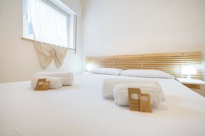 A hotel room with a large bed, two bedside tables, a window with curtains, and a wooden headboard. - Debora's Flat (Verona)