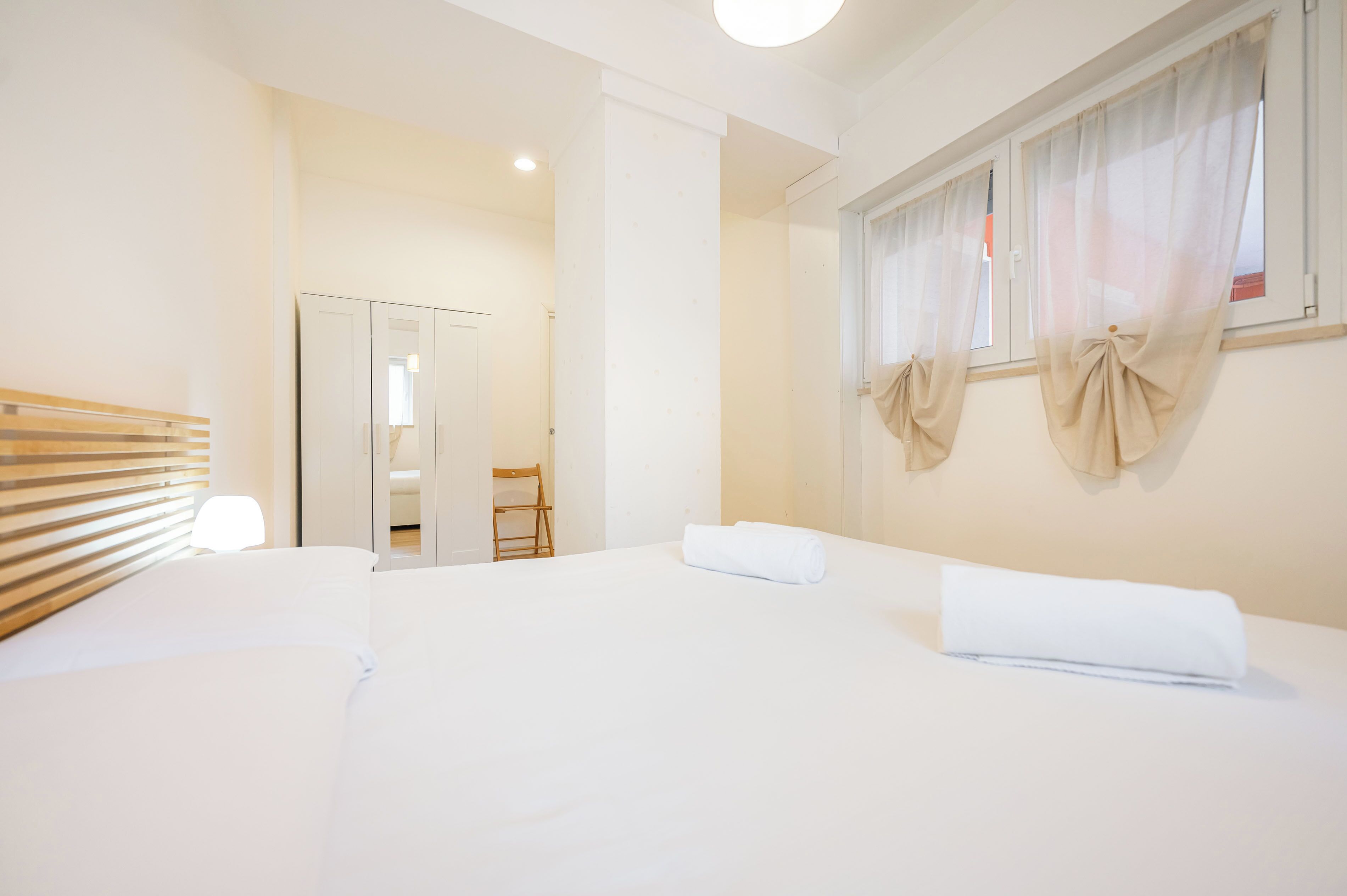 Hotelkamer met een bed, een houten hoofdeinde, een stoel, een kledingkast en een raam met gordijnen.