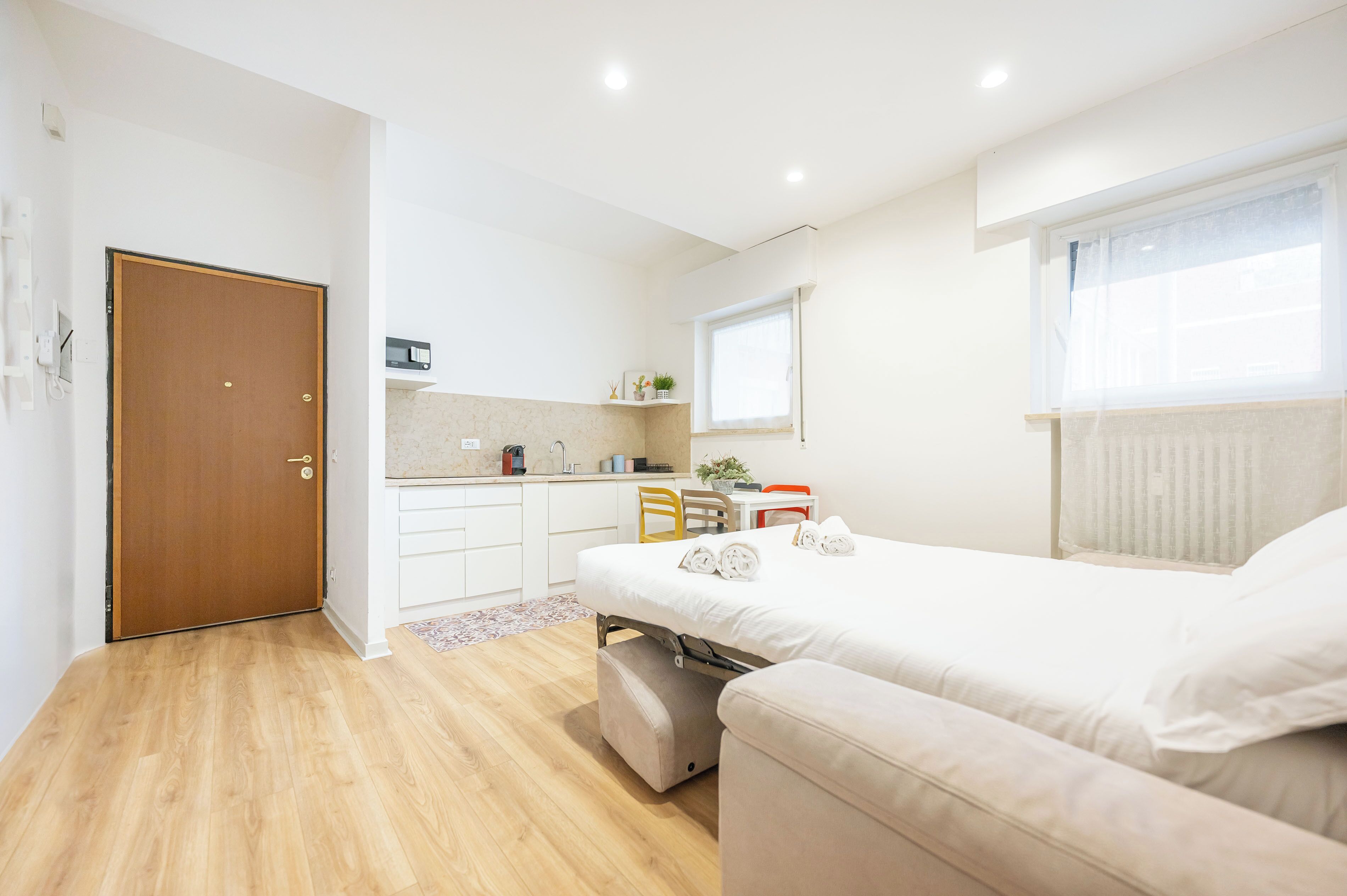 Une pièce de taille modeste comprenant un lit, une petite kitchenette, une fenêtre avec des stores et une porte.
