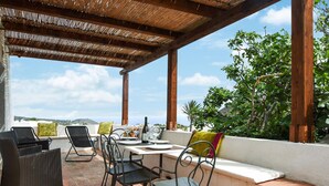 Eine Terrasse im Freien mit Korbmöbeln, einem Esstisch und Blick auf die Landschaft.