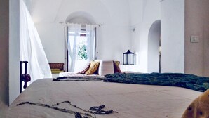 Ein Schlafzimmer mit einem großen Bett, einem Fenster mit durchsichtigen Vorhängen, einem Nachttisch und einer Wandlampe.