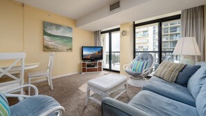 A living room with a television, wicker furniture, a sofa, and a view of a building through large windows.
