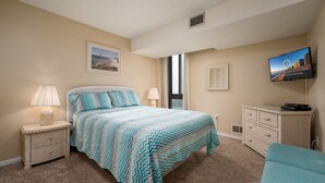 A bedroom with a bed, a nightstand, a dresser, a television, and a window.