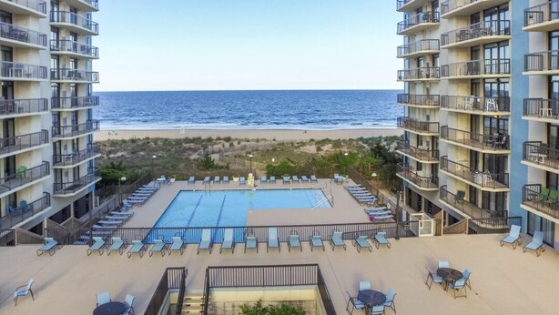 A hotel with a pool, lounge chairs, and a view of the ocean.