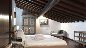 A bedroom with a large bed, a wooden ceiling, a green cabinet, and a painting on the wall.