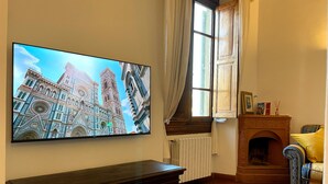A living room with a large TV displaying a cityscape, a fireplace, and a vintage sofa.