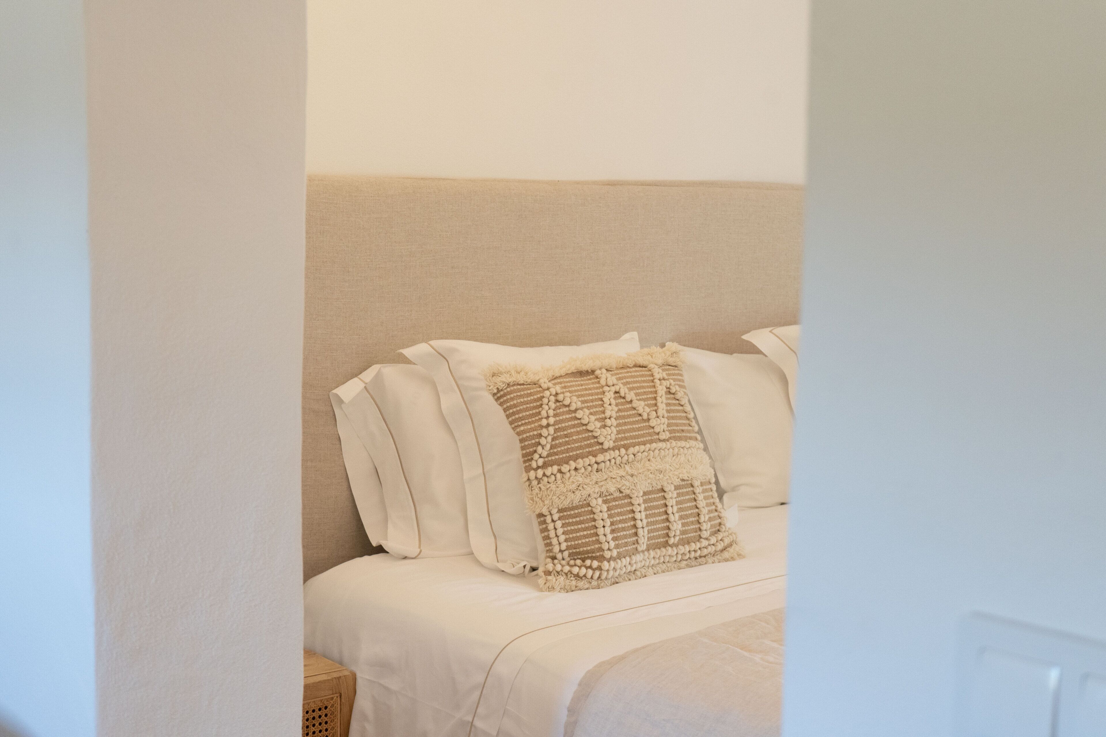 Una cama con ropa de cama blanca y un cojín decorativo con textura.