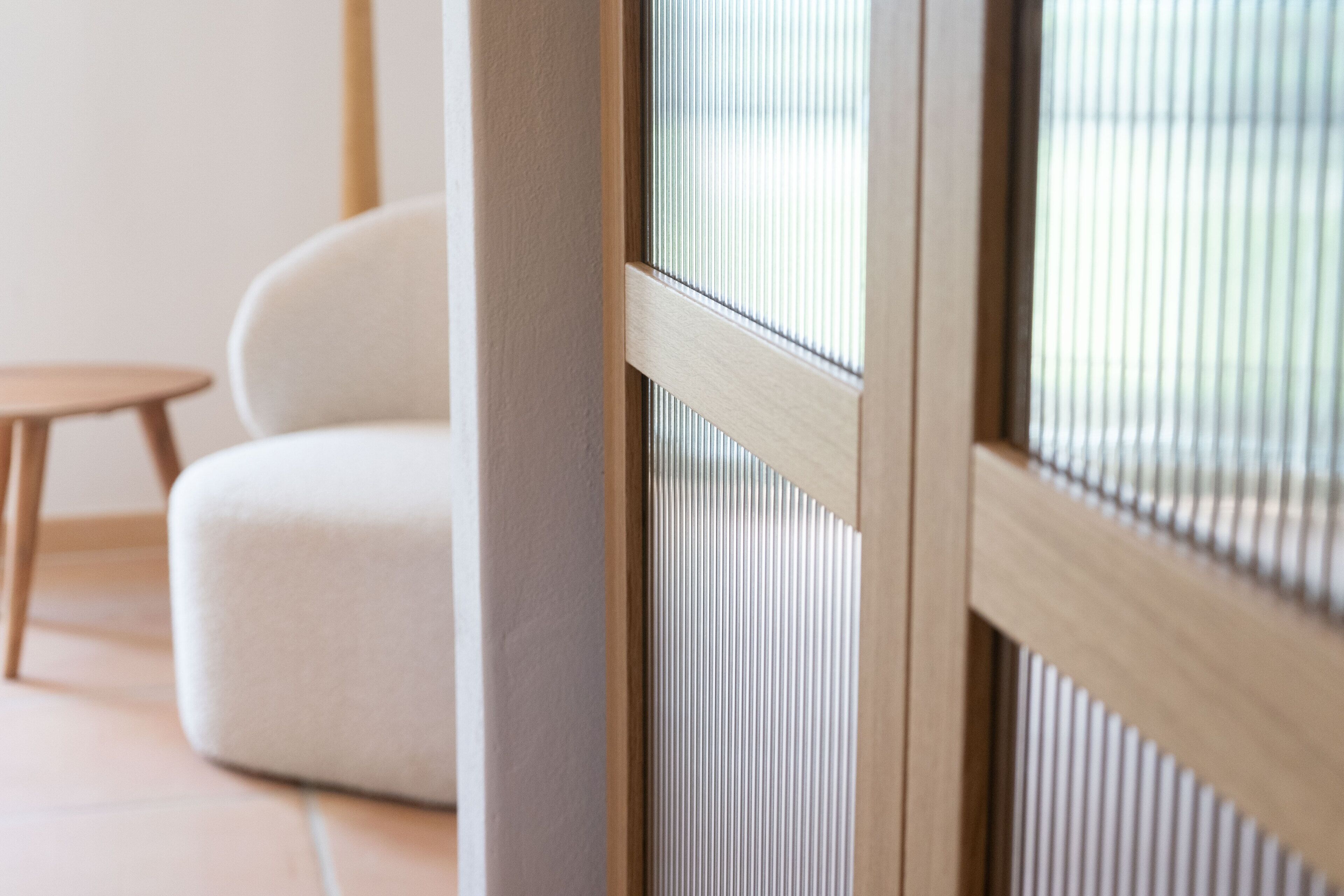 Una habitación con ventana de madera, un sofá blanco y una pequeña mesa de madera.