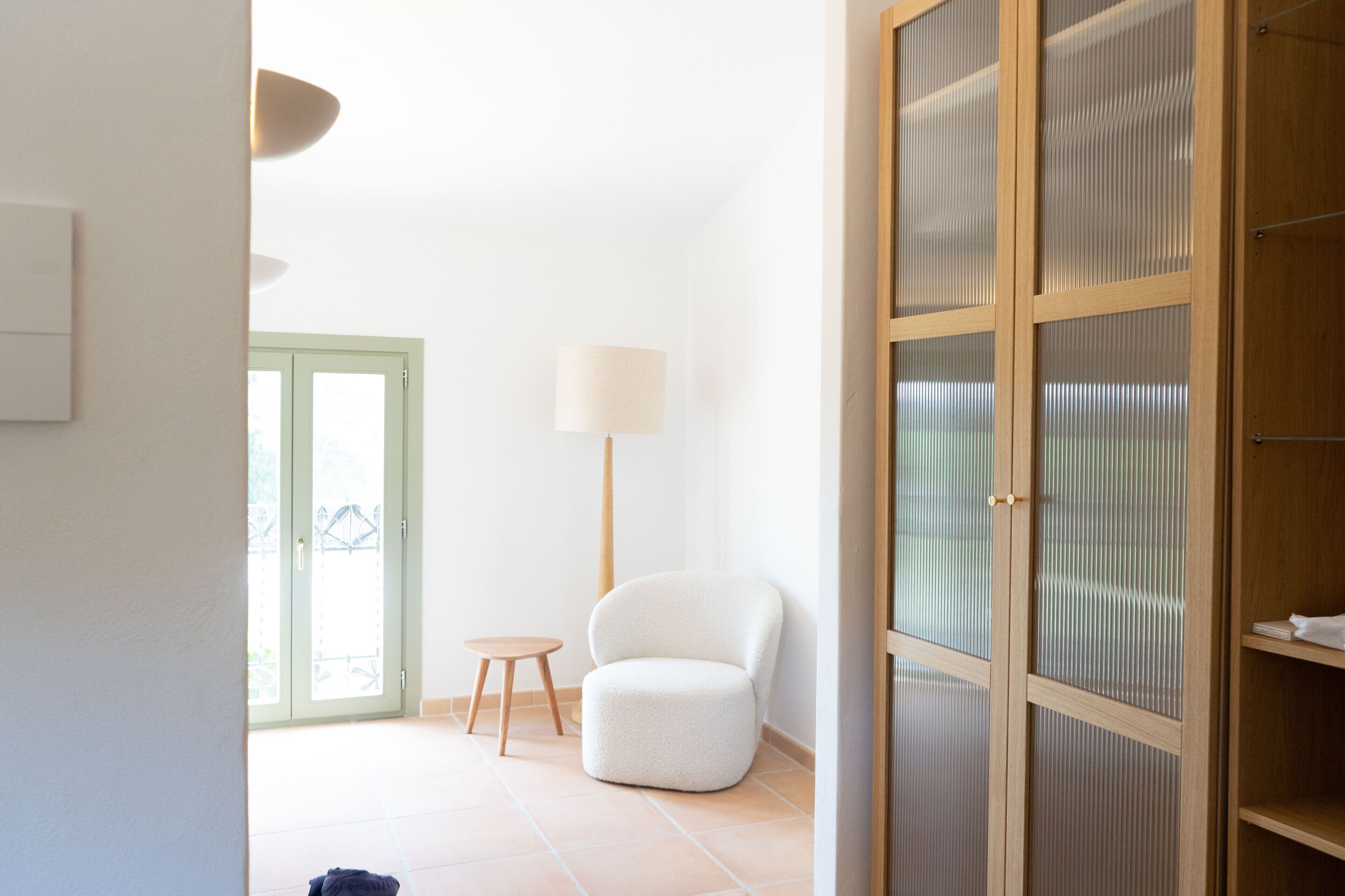 A room with a sliding door, a small round table, a white chair, a lamp, and a wooden cabinet.