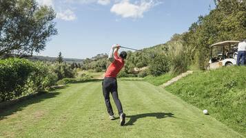 Una persona juega al golf en un campo bien cuidado con cielo despejado.