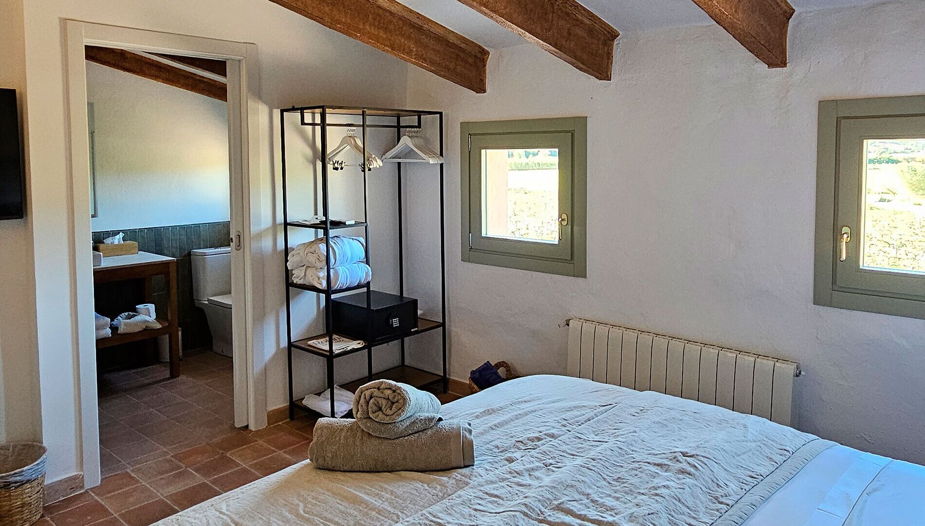 Un dormitorio con cama, radiador, ventana y baño con inodoro y estanterías.
