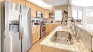 Una cocina moderna con electrodomésticos de acero inoxidable, armarios de madera y encimeras de granito, además de un lavamanos grande.