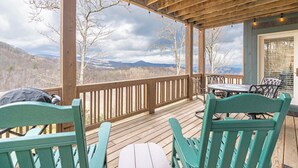 Una terraza de madera con mobiliario exterior, una mesa y vistas a las montañas.