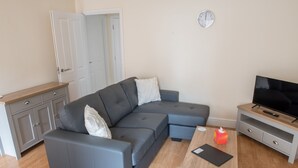 Ein modernes Wohnzimmer mit einem grauen Ecksofa, einem Holztisch, einem Flachbildfernseher und einem grauen Schrank.