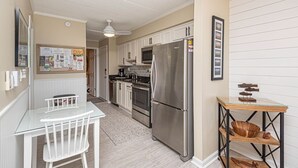 A compact kitchen with white cabinetry, a stainless steel refrigerator, and a small dining table with chairs.